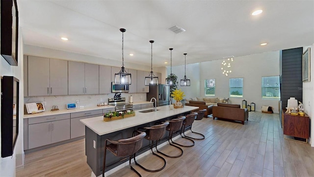 kitchen featuring appliances with stainless steel finishes, a kitchen breakfast bar, a center island with sink, light hardwood / wood-style flooring, and gray cabinets