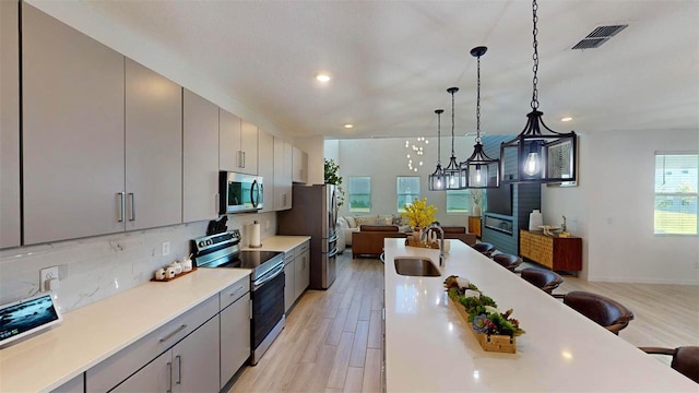 kitchen with a kitchen bar, gray cabinetry, stainless steel appliances, sink, and a chandelier