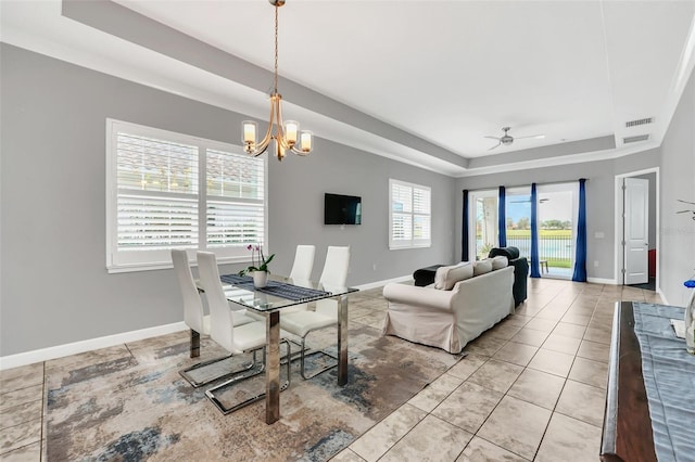 dining area with ceiling fan with notable chandelier, a tray ceiling, and light tile patterned flooring