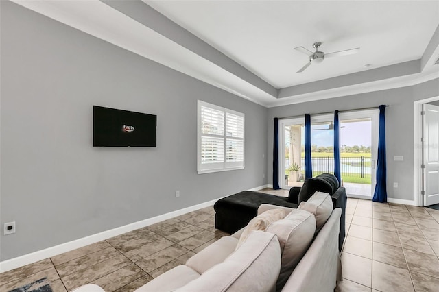 living room featuring a tray ceiling, ceiling fan, and light tile patterned floors