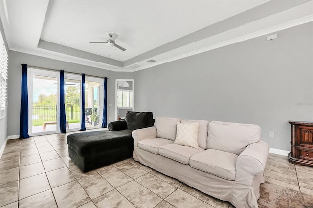 living room featuring a raised ceiling, ceiling fan, light tile patterned floors, and ornamental molding