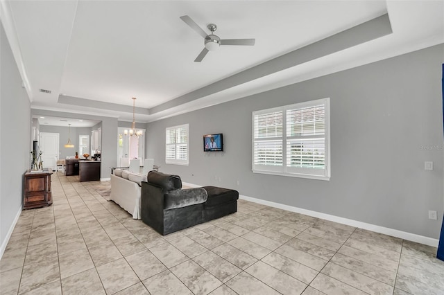 living room with ceiling fan with notable chandelier and a raised ceiling