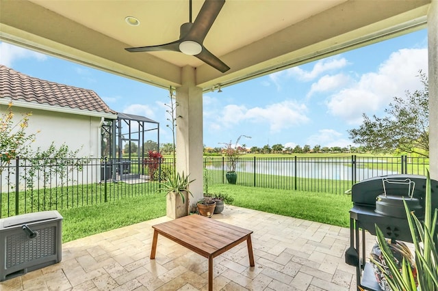 view of patio featuring ceiling fan, a grill, a water view, and glass enclosure