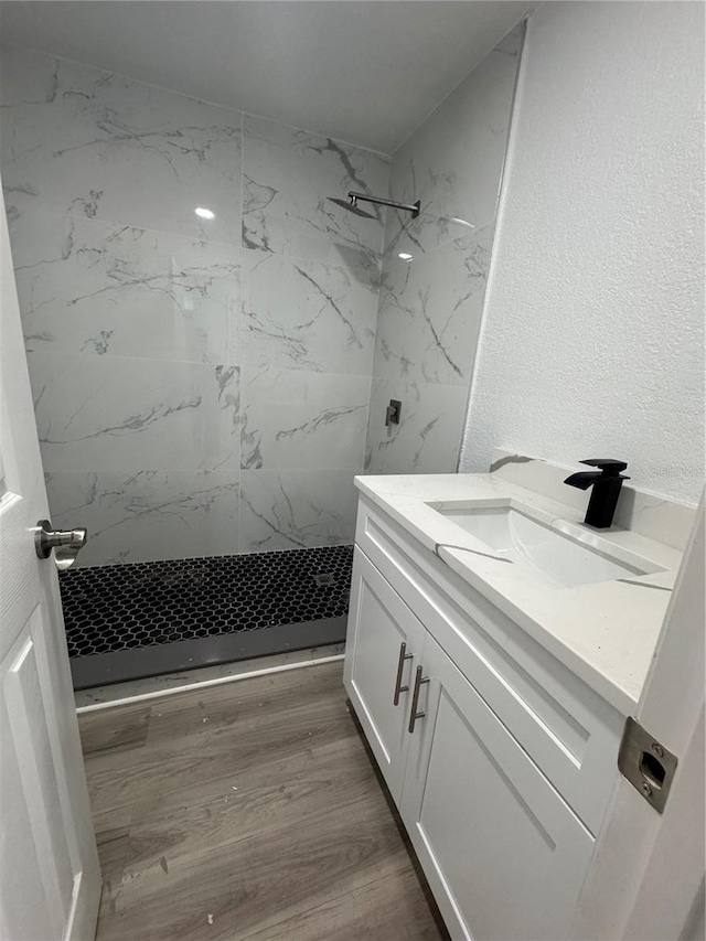 bathroom with hardwood / wood-style flooring, vanity, and a tile shower