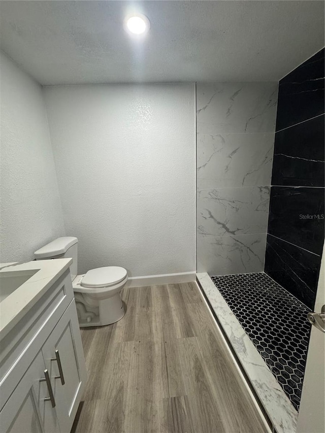 bathroom with vanity, toilet, a textured ceiling, tiled shower, and wood-type flooring