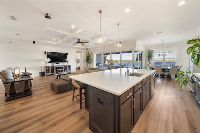 kitchen with coffered ceiling, dark brown cabinets, sink, light hardwood / wood-style floors, and an island with sink