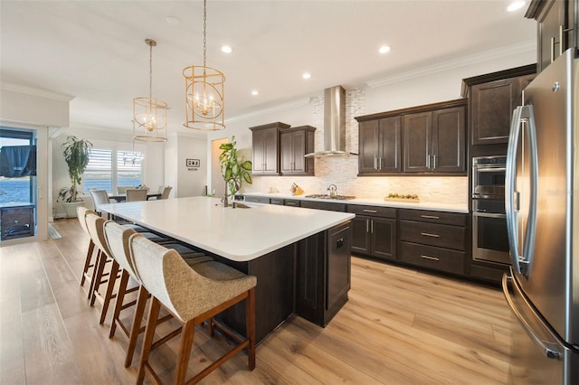 kitchen with decorative light fixtures, stainless steel appliances, wall chimney exhaust hood, and light hardwood / wood-style floors