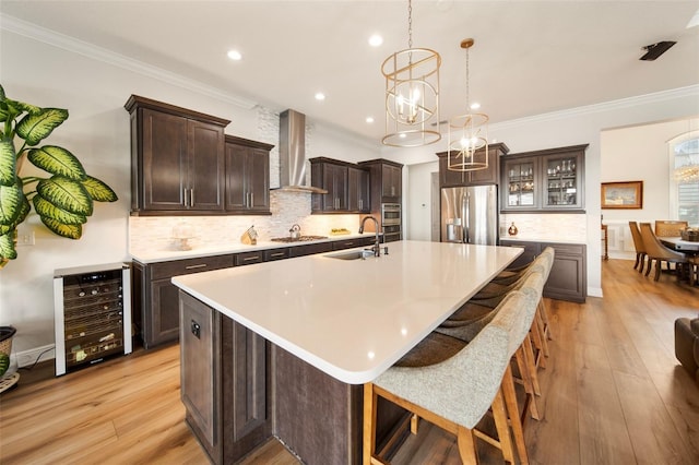 kitchen featuring wall chimney range hood, sink, light hardwood / wood-style flooring, stainless steel appliances, and beverage cooler