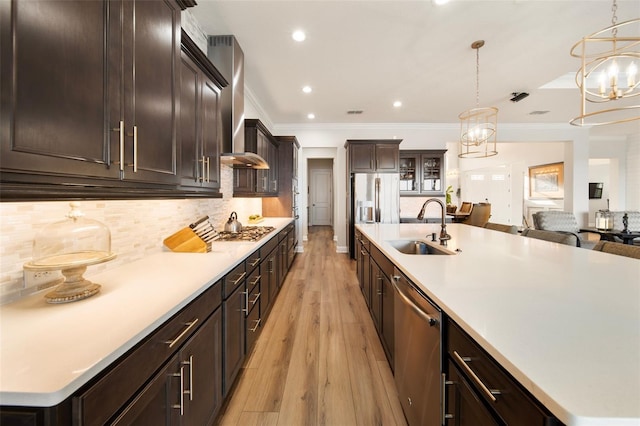 kitchen with a large island, sink, wall chimney exhaust hood, light hardwood / wood-style floors, and appliances with stainless steel finishes