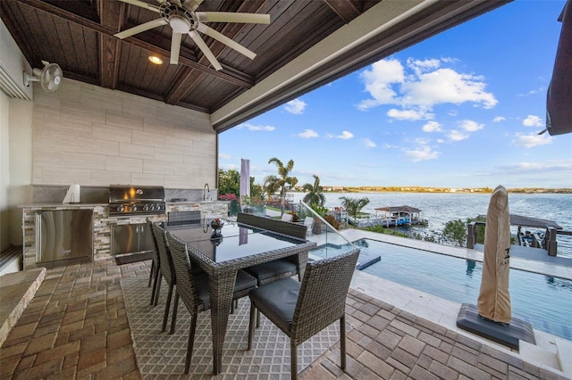 view of patio / terrace featuring an outdoor kitchen, ceiling fan, sink, a water view, and grilling area