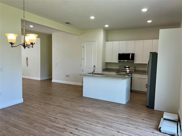 kitchen featuring appliances with stainless steel finishes, pendant lighting, light hardwood / wood-style floors, white cabinetry, and an island with sink