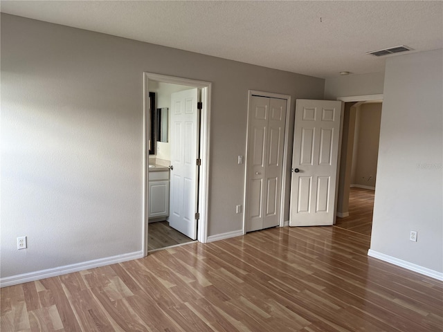 unfurnished bedroom featuring hardwood / wood-style floors, a textured ceiling, and ensuite bathroom