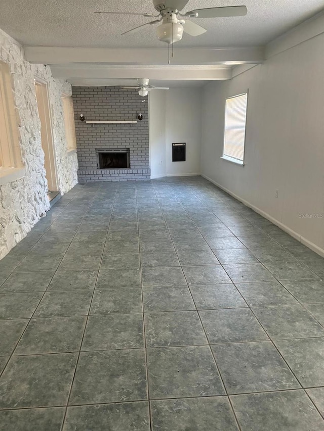 unfurnished living room featuring dark tile patterned flooring, ceiling fan, a fireplace, a textured ceiling, and beamed ceiling