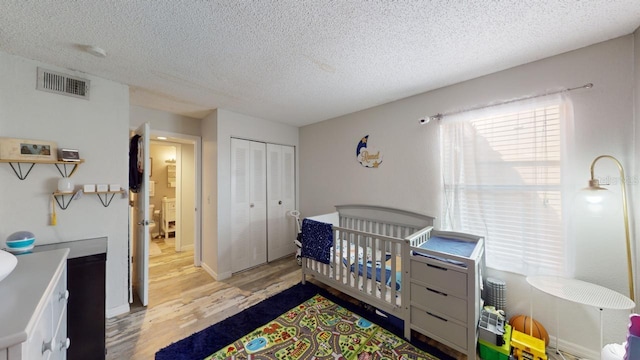 bedroom with a textured ceiling, a crib, light hardwood / wood-style flooring, and a closet