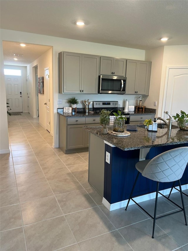 kitchen with stainless steel appliances, dark stone countertops, gray cabinets, a breakfast bar area, and light tile patterned flooring