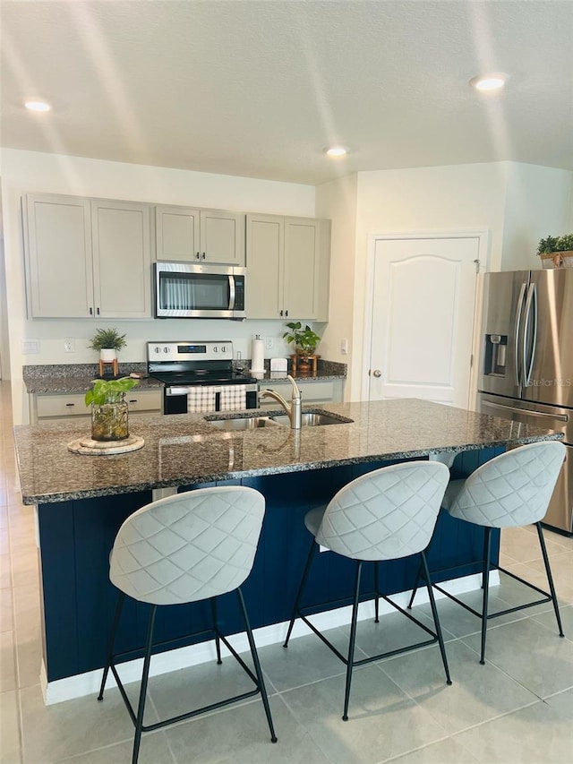 kitchen featuring a sink, dark stone counters, a kitchen bar, and appliances with stainless steel finishes