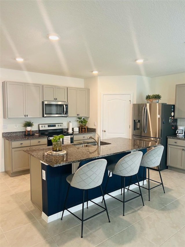 kitchen featuring gray cabinets, appliances with stainless steel finishes, a breakfast bar, and a sink