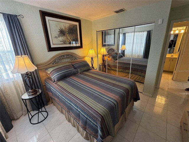 tiled bedroom featuring a textured ceiling, multiple windows, and ensuite bath