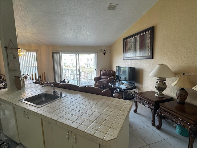 kitchen featuring tile countertops, sink, light tile patterned floors, a textured ceiling, and kitchen peninsula