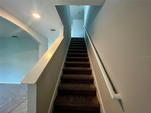 staircase with a textured ceiling and carpet floors