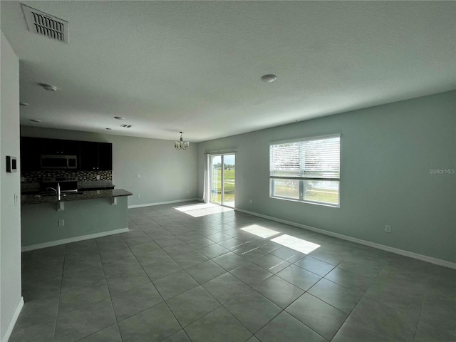 unfurnished living room featuring tile patterned flooring, a textured ceiling, and an inviting chandelier