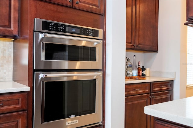 kitchen featuring decorative backsplash, light stone counters, and stainless steel double oven