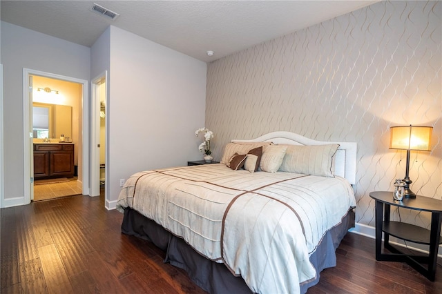 bedroom with a textured ceiling, ensuite bath, and dark hardwood / wood-style floors