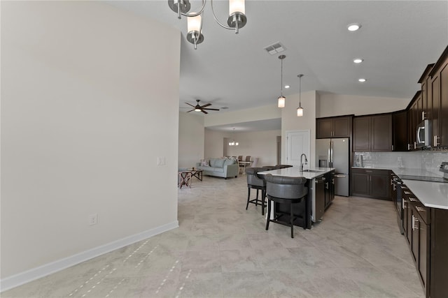 kitchen with a kitchen breakfast bar, dark brown cabinets, stainless steel appliances, vaulted ceiling, and a center island with sink