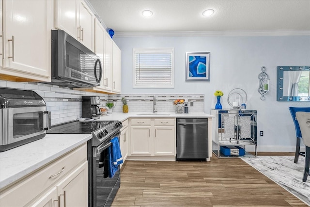 kitchen with black appliances, white cabinetry, ornamental molding, and sink