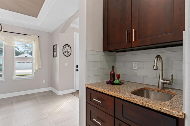 kitchen with light stone countertops, decorative backsplash, sink, dark brown cabinets, and crown molding