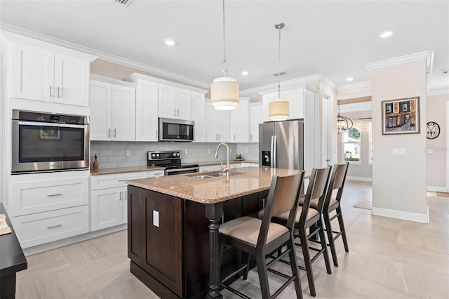 kitchen with a center island with sink, sink, hanging light fixtures, appliances with stainless steel finishes, and white cabinets