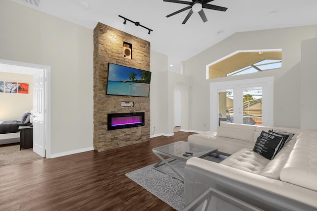 living room with high vaulted ceiling, track lighting, a stone fireplace, ceiling fan, and dark hardwood / wood-style flooring