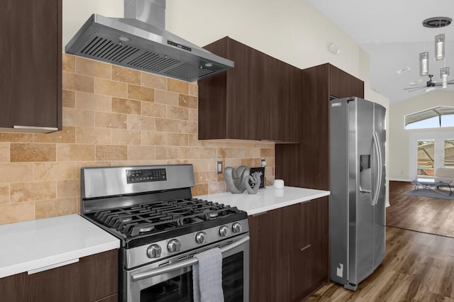 kitchen with ceiling fan, wall chimney exhaust hood, pendant lighting, appliances with stainless steel finishes, and light wood-type flooring