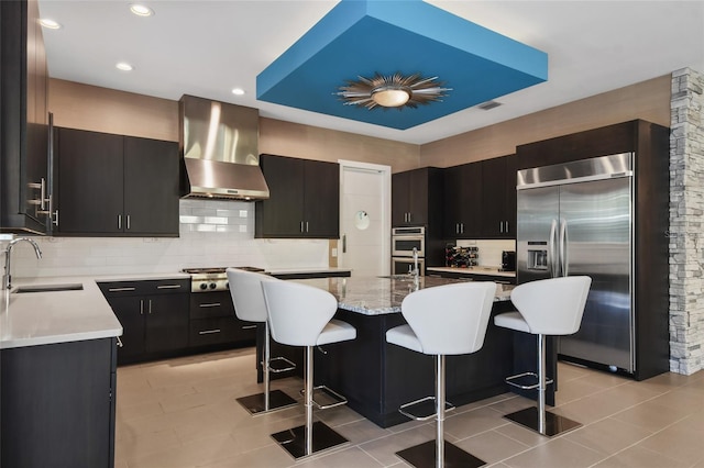 kitchen featuring a center island with sink, a kitchen breakfast bar, ventilation hood, sink, and appliances with stainless steel finishes