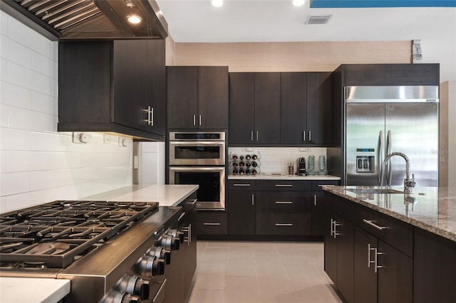 kitchen featuring custom exhaust hood, sink, appliances with stainless steel finishes, tasteful backsplash, and light stone counters