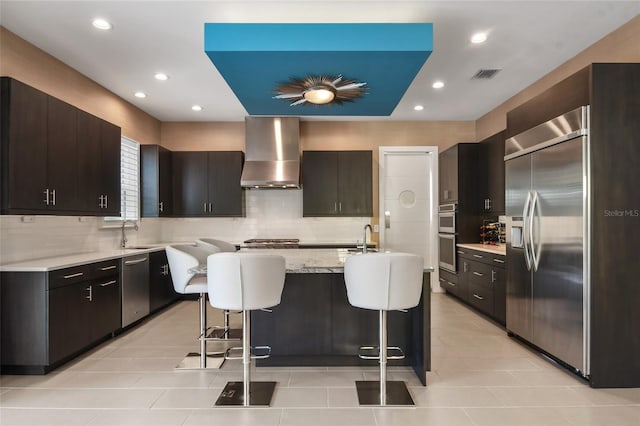 kitchen featuring a breakfast bar, wall chimney range hood, sink, a kitchen island, and stainless steel appliances