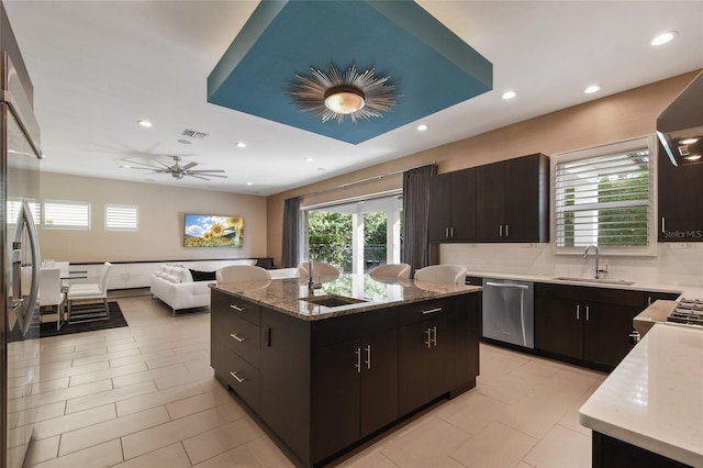 kitchen featuring appliances with stainless steel finishes, backsplash, ceiling fan, sink, and an island with sink