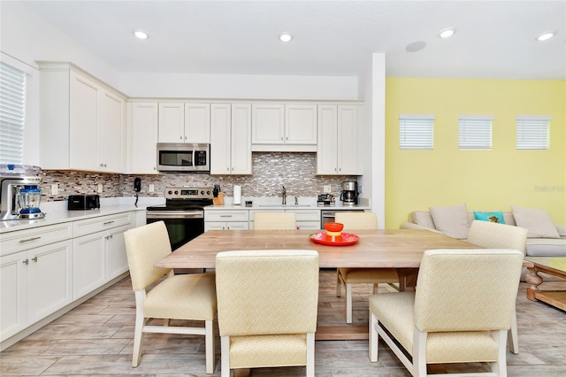 kitchen featuring white cabinetry, sink, stainless steel appliances, backsplash, and a breakfast bar area