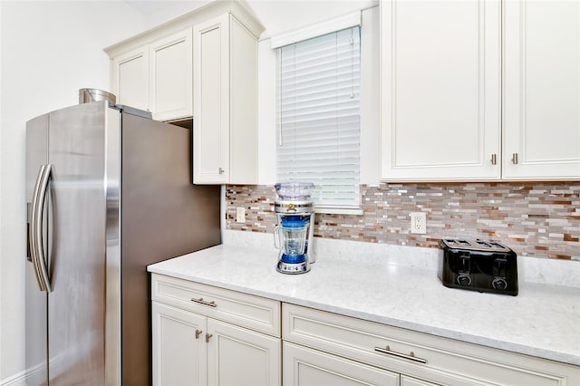 kitchen featuring backsplash, stainless steel fridge, and light stone counters