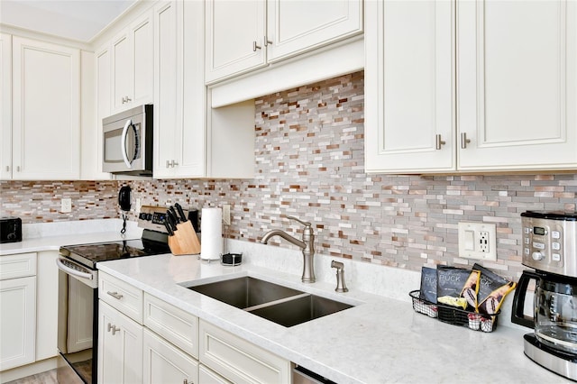 kitchen with white cabinets, sink, decorative backsplash, light stone counters, and stainless steel appliances