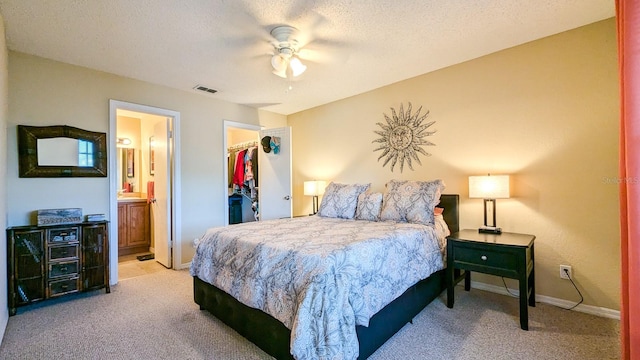 carpeted bedroom with a walk in closet, a textured ceiling, ceiling fan, connected bathroom, and a closet