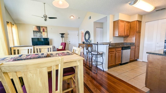 kitchen featuring light wood-type flooring, a textured ceiling, ceiling fan, dishwasher, and lofted ceiling