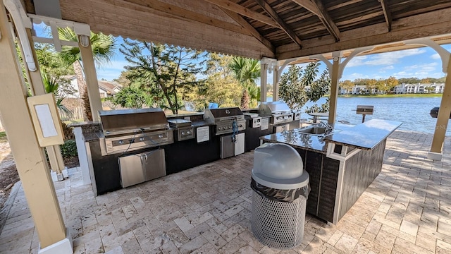 view of patio / terrace featuring a gazebo, a water view, grilling area, and exterior kitchen