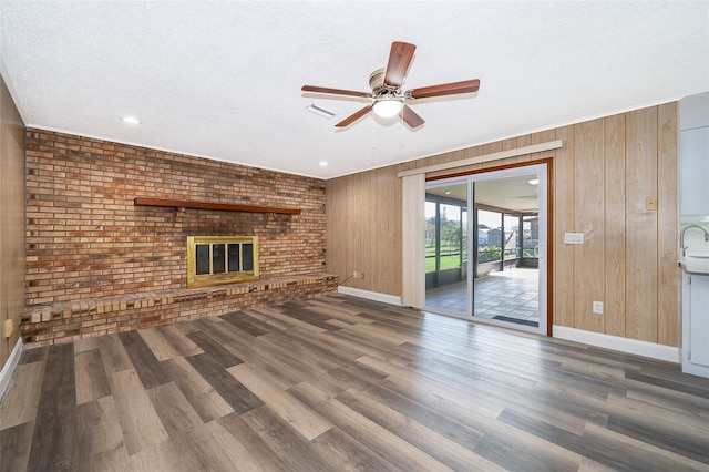 unfurnished living room featuring a brick fireplace, brick wall, a textured ceiling, dark hardwood / wood-style floors, and wood walls