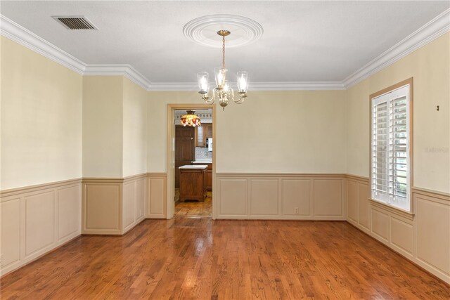 spare room featuring light hardwood / wood-style flooring, ornamental molding, and a notable chandelier