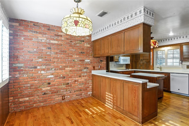 kitchen with pendant lighting, white appliances, light hardwood / wood-style floors, kitchen peninsula, and brick wall