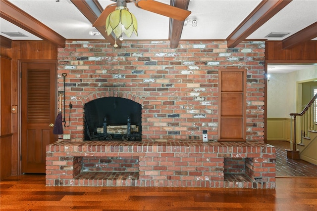 living room featuring beam ceiling, dark hardwood / wood-style flooring, wooden walls, and a brick fireplace