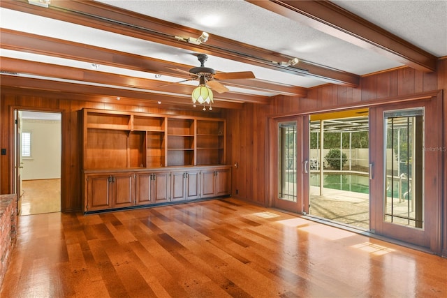 unfurnished living room featuring ceiling fan, beamed ceiling, hardwood / wood-style floors, a textured ceiling, and wooden walls