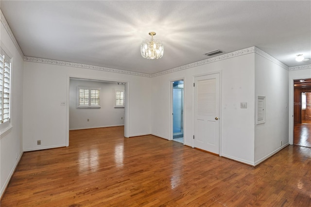 unfurnished room featuring wood-type flooring, ornamental molding, and a notable chandelier