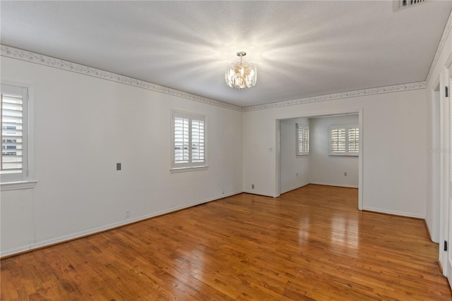 unfurnished room with a textured ceiling, a wealth of natural light, a notable chandelier, and light wood-type flooring